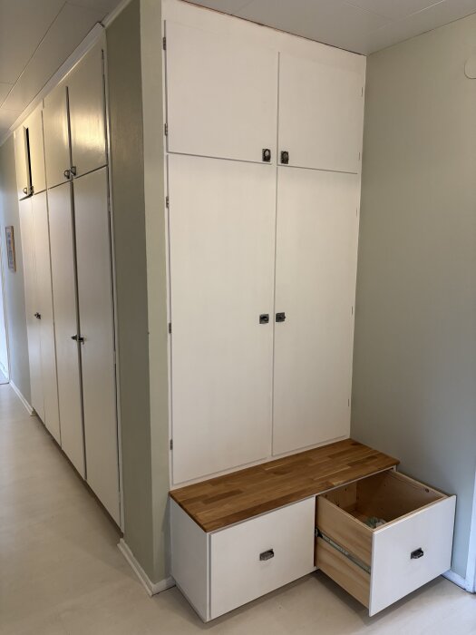 Vit garderob med två sektioner byggd mot vägg, originaldel till vänster och sektion med sittbänk och utdragbar låda till höger.