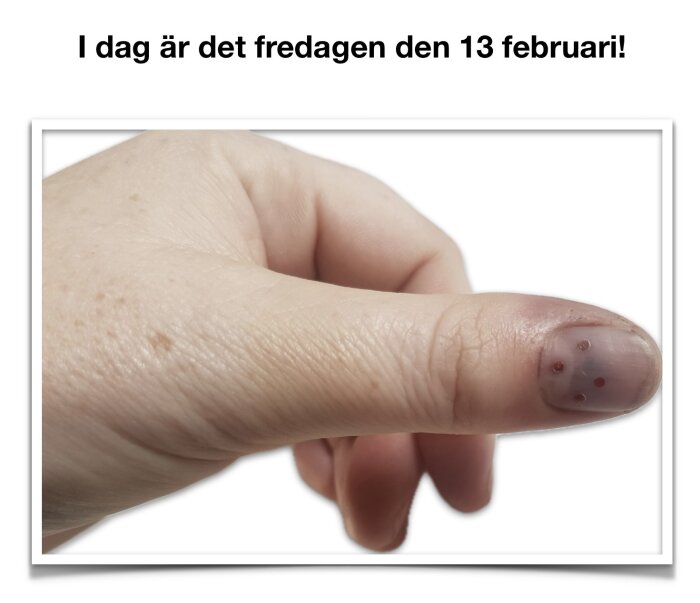 Hand med tummen upp, nageln har små dekorationer. Text ovanför: "I dag är det fredagen den 13 februari!