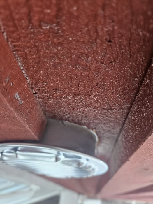 Ventilgaller monterat under en röd träbottenbräda, sticker ut något.