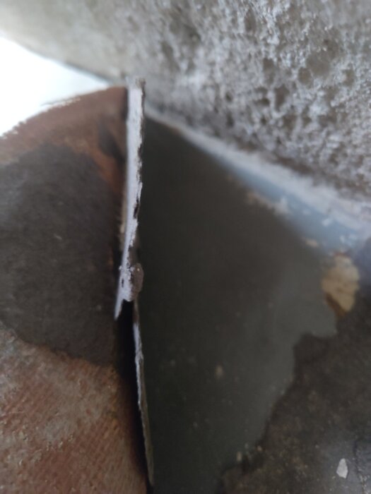 Närbild av golvlager i källare med betong, linoleummatta och tunt svart skikt som liknar filtmatta, potentiellt innehållande asbest.