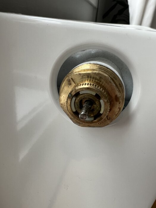Termostatventil på en vit radiator med synlig mässingsdetalj och något markerat märke eller nummer på ventilen.