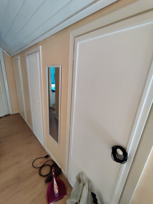 Tre vita garderobsdörrar i ett rum med ljusbruna väggar. En spegel är fäst på en dörr, och en purpurfärgad sopskyffel står på golvet.