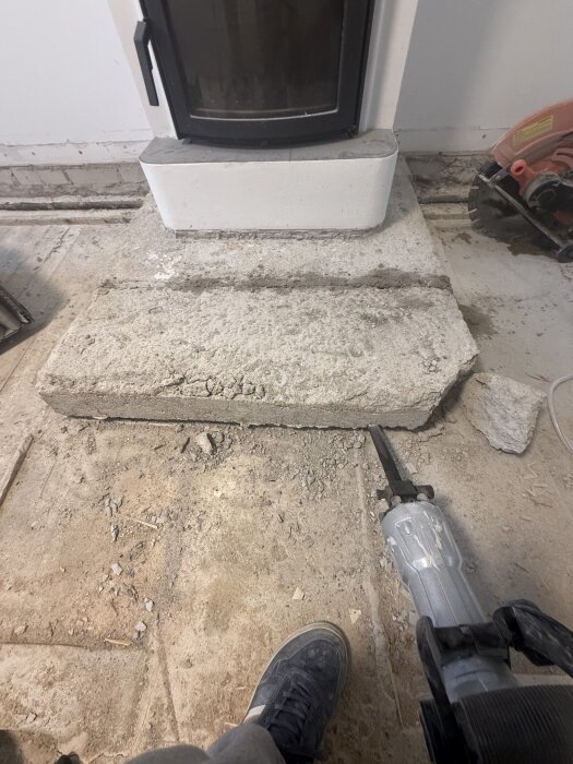 Kamin med nedkortad sula, golvet är dammigt från byggarbete. En såg och en fot med sko syns i förgrunden.