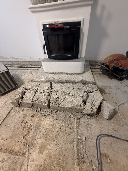 Krossad cementplatta framför en kamin efter att golvet kortats ner med 40 cm; byggverktyg syns vid sidan.