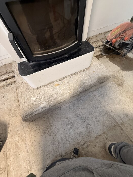 En kamin med kortad stensula framför, samt en cirkelsåg på golvet intill.