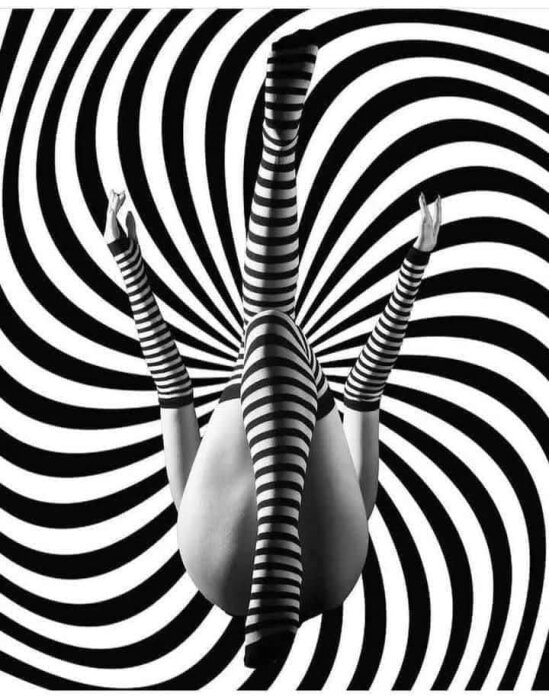 Person i randiga strumpor poserar mot en svartvit spiralbakgrund, vilket skapar en optisk illusion.