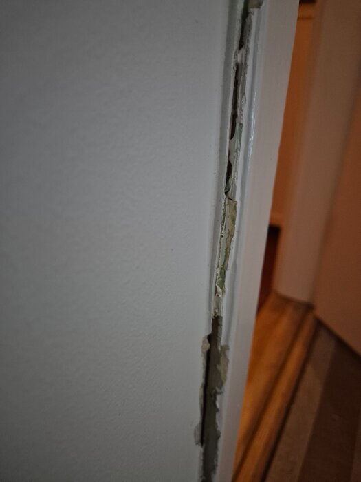 Sprucket färg- och tapetlager längs en dörrkarm visar borttagna kablar och ojämn yta att slipa och spackla.