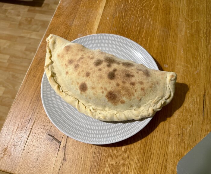 Hemgjord calzone-pizza på en mönstrad tallrik, bakad efter handknådad deg som jästs en timme.