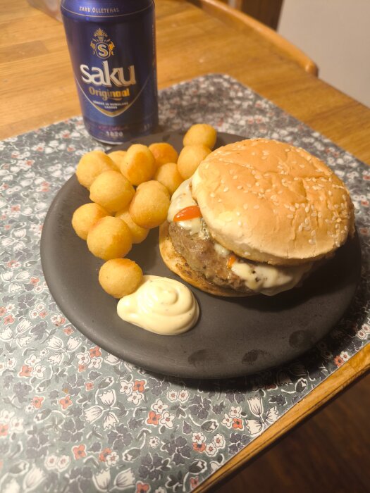 Högrevsburgare med dressing, stekt lök, jalapeno, chilisås och ost, serverad med kroketter, bea och öl på ett blommigt underlägg.