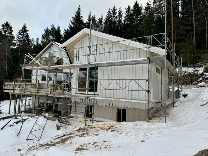 Bygget av ett vitt hus med ställningar kring fasaden i en snötäckt miljö, omgivet av skog.