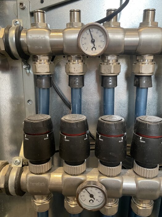Termometrar och ventiler på ett rörsystem för radiatorer, visar temperaturer och inställningar.