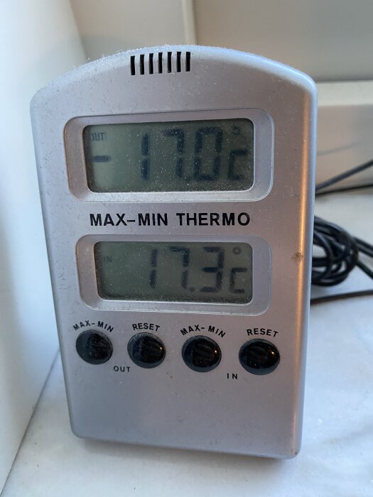 Digital termometer som visar utetemperaturen -17,0°C och inomhustemperaturen 17,3°C, placerad på en fönsterbräda.