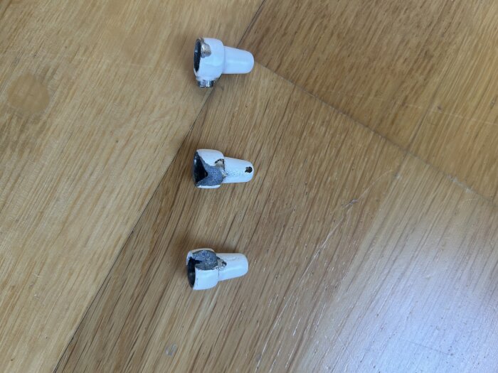 Tre trasiga vita golvskydd på ett trägolv i mörkare nyans. Golvskydden ser slitna och skadade ut.