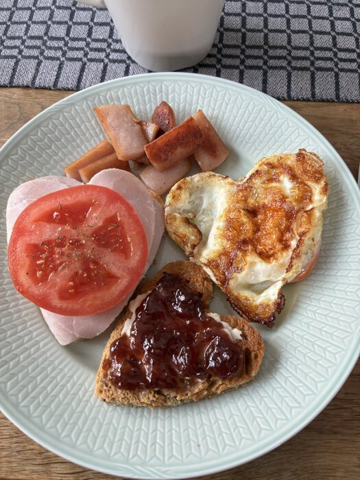 Hjärtaformat stekt ägg och rostat bröd med sylt, köttskiva med tomat, stekt korv på en tallrik. Ingen kopp synlig förutom överkanten.