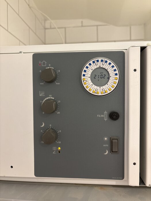 Kontrollpanel på Nibe EVC13 med temperaturinställning och klockdisplay, med ett finger som pekar mot reglagen.