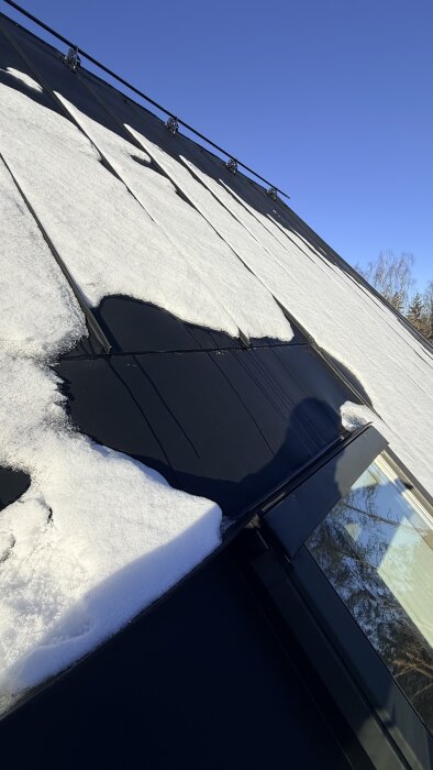 Snötäckt tak med pågående snösmältning och läckande takfönster, soligt väder och blå himmel i bakgrunden.