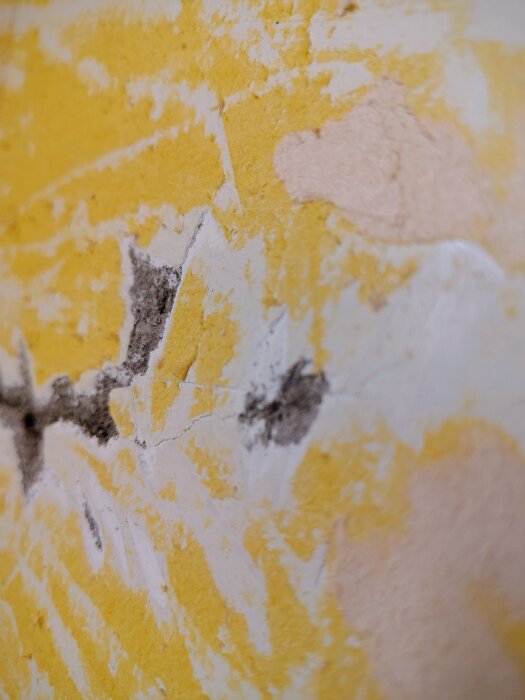 Close-up of a textured yellow and white wall surface with cracks and black marks.