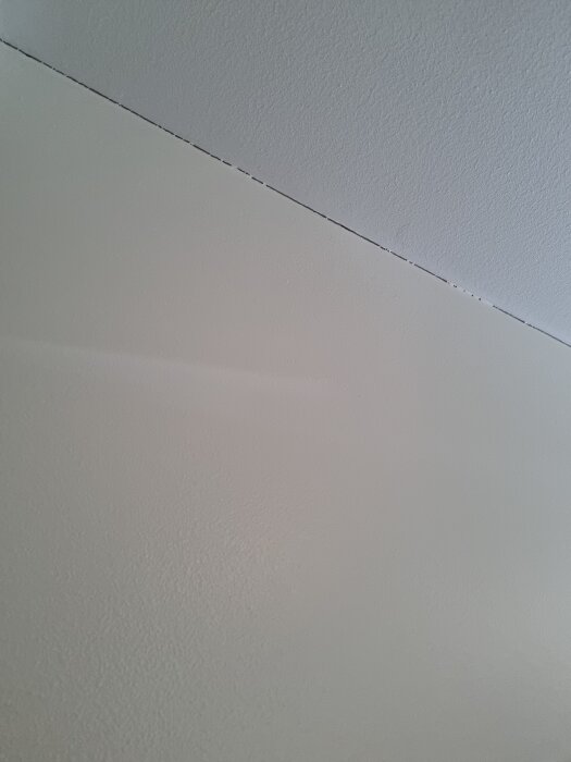 Spricka mellan vitt innertak och vägg utan taklist i ett renoverat hus, med fokus på sprickbildningens omfattning.