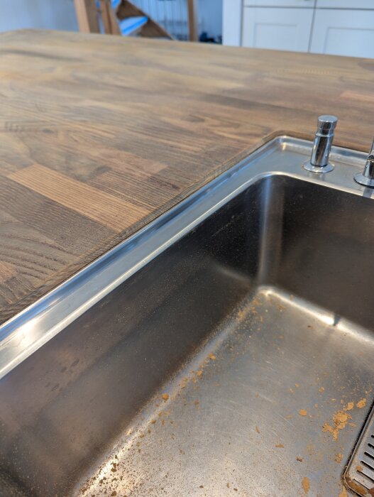 Träbänkskiva med diskho i rostfritt stål, lätt smutsad, i ett kök med vita skåp i bakgrunden.