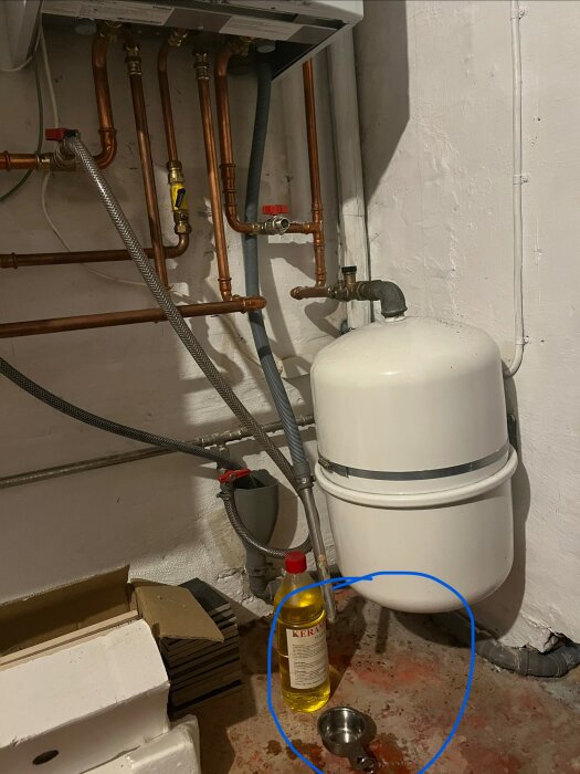 Rör kopplade till panna med dropp från grått rör; mätkopp och rengöringsflaska på golvet.