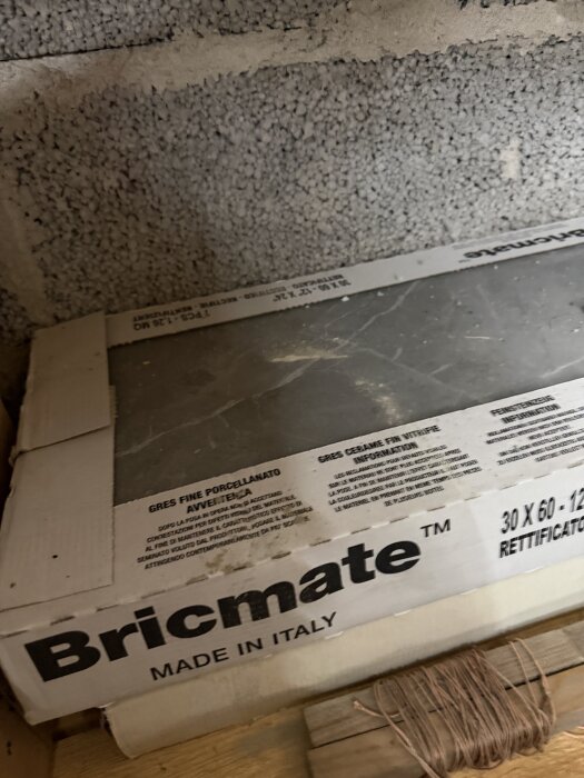 En kartong med Bricmate kakel märkt "Made in Italy" står lutad mot en vägg av lättbetongblock.