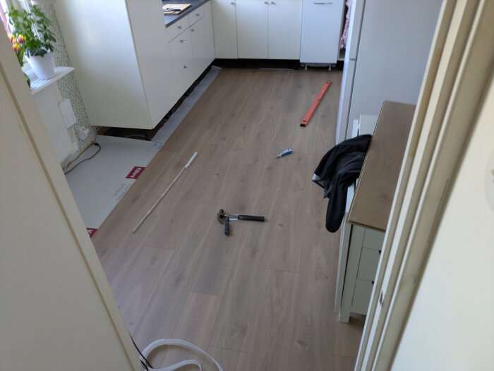 Kök under renovering med nytt golv på plats, verktyg på golvet och möbler flyttade för att underlätta golvläggningen.
