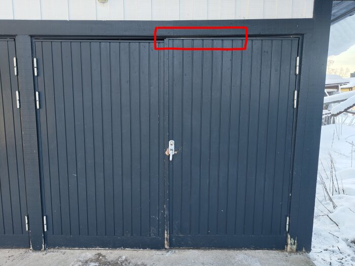 Garagedörr med höger dörrblad som kärvar, markerat område där dörren tar i karmen i ovankant. Omgivning med snö.