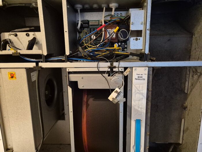 Ventilationssystem med exponerade kablar och filterinsats, visar enhetens inre komponenter och teknik.