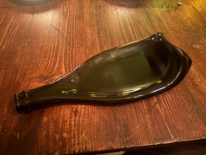 Platt smält glasflaska på ett bord av trä.