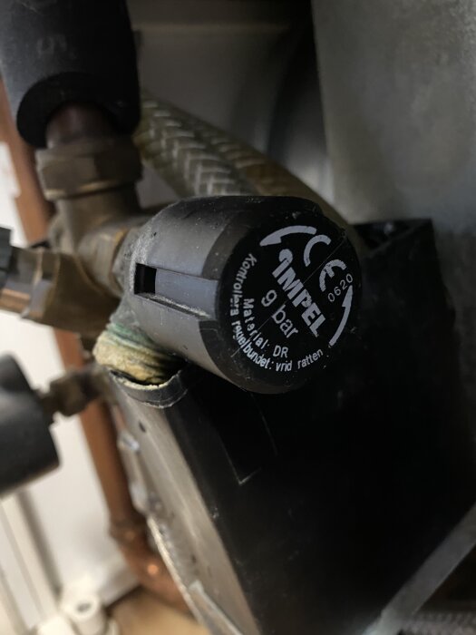 Närbild på en läckande ventil eller koppling på en IVT690 från märket Impel, med text och symboler synliga på ventilen.