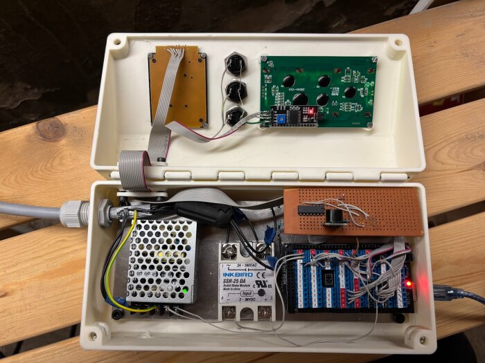 Öppen styrbox för keramikugn med elektroniska komponenter och kablar, inklusive en styrenhet, kopplingskort och displaypanel monterade i en plastlåda.