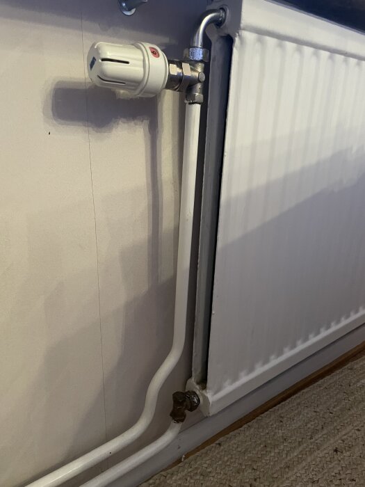 Radiator med vita rör och termostatventil, ansluten till väggen utan tejp.