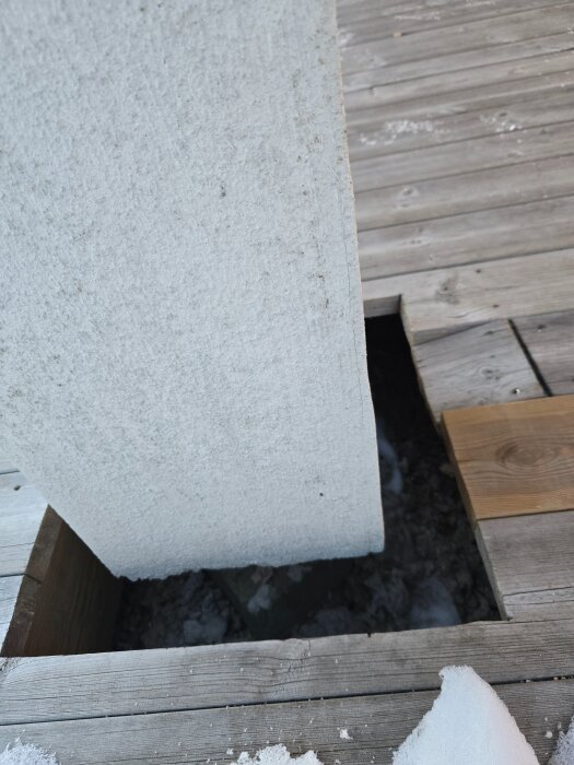 Putsskadad pelare med hörnlister och överlappande nät intill plankgolv med snö. Problematik med sprickbildning i hörn.