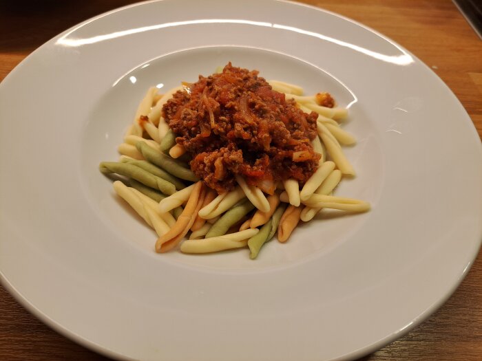 Färgglad pasta med köttfärssås serverad på en vit tallrik.