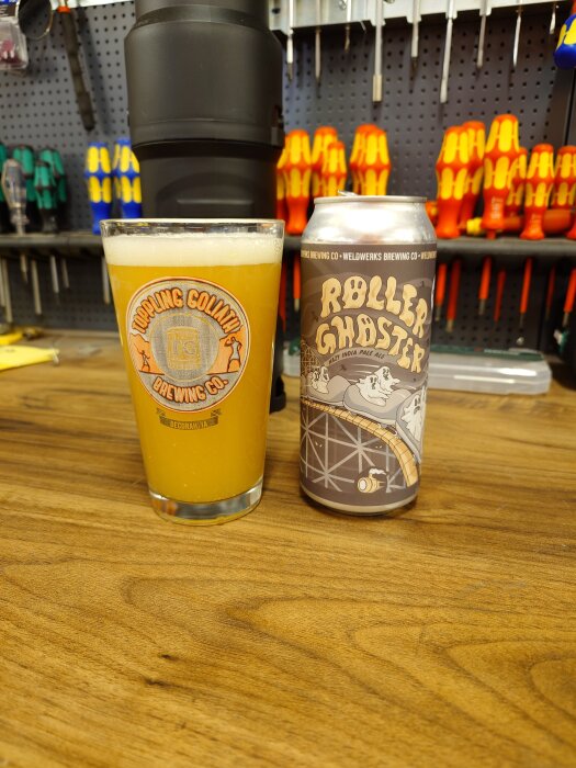 En ölburk märkt "Roller Ghoster" och ett ölglas med gyllene IPA står på en bänkskiva i ett verkstadsmiljö med verktyg i bakgrunden.