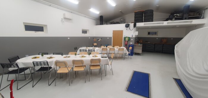 Ett garage med bord dukade för event, stolar runt borden, däck staplade på loftet och arbetsbänkar längs väggen.