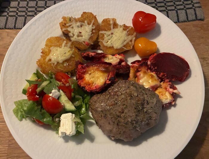 Lamm med potatishjärtan, rödbetsgratäng med chèvre, sallad med tomat, gurka, salladsblad och fetaost, serverat på en vit tallrik.