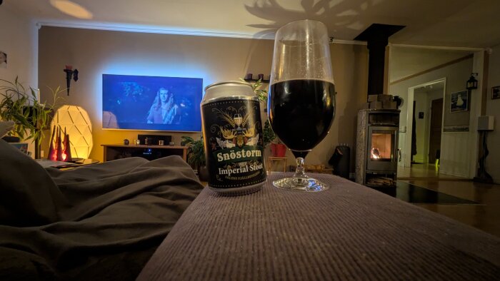 Snöstorm Imperial Stout-burk och full glas framför en TV som visar Braveheart, med tänd brasa i bakgrunden.