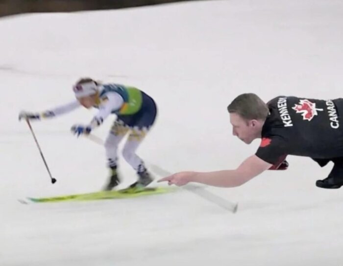 Skidåkare i tävling, en person från Kanada ser ut att sopa före åkaren, humoristisk kombination av längdskidåkning och curling.