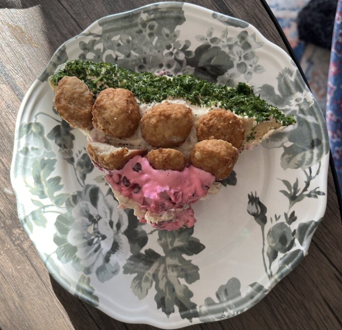 Hjärttformad smörgåstårta toppad med köttbullar och grönsaker på ett blommigt fat.