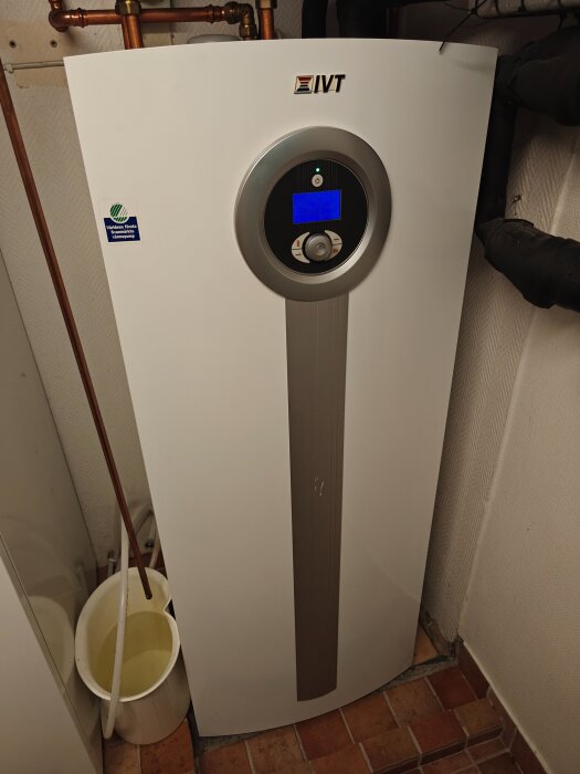 IVT värmepump i ett rum med kopparrör och en vit hink fylld med vatten bredvid. Inget synligt fel på elektroniken.