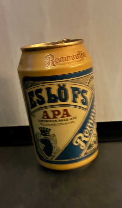 En burk Eslöfs APA American Pale Ale med etikett i blått och guld, fotograferad på ett bord.