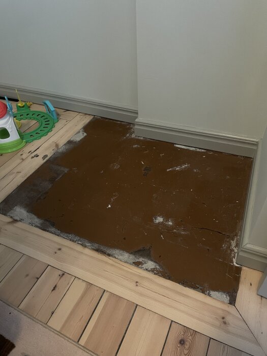 En stenplatta inomhus, omgiven av trägolv, som delvis är lagad med putsbruk.