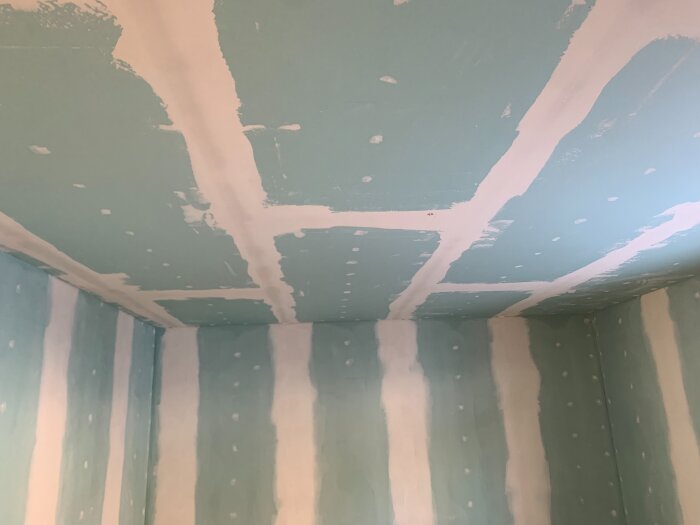 Tak och väggar med gipsplattor har fogas och spacklats, med pågående spackling och slipning i ett rum under renovering.