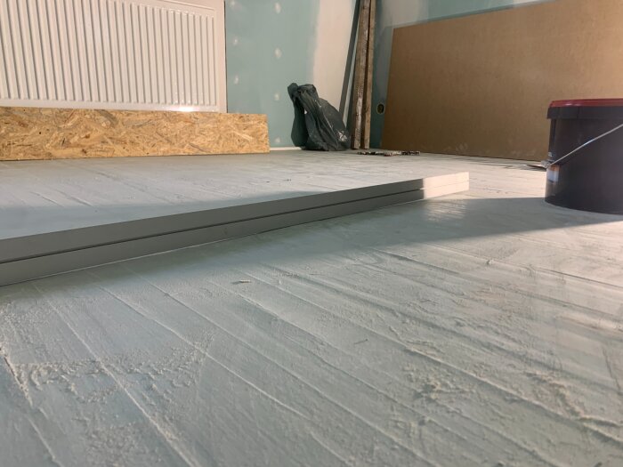 Renovering pågår med målat golv och brädor, samt verktyg och material i bakgrunden.