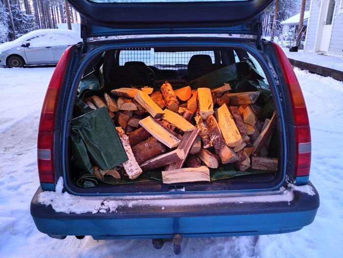 Bakluckan på en bil fylld med ved i ett snöigt landskap.