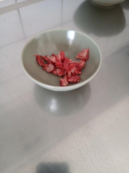 En skål med bitar av rått kött på ett bord.