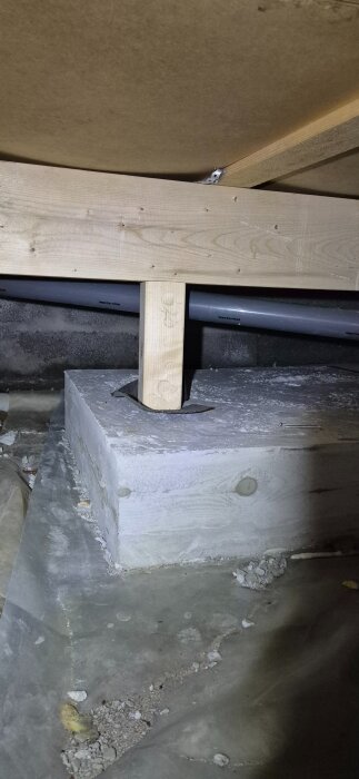 Förstärkning i krypgrund med träsupport på betongblock, omgiven av rör och dammiga ytor.
