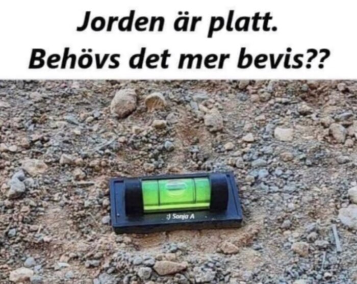 Vattenpass som visar vågrätt mark på grusig yta med texten 'Jorden är platt. Behövs det mer bevis??' ovanför.