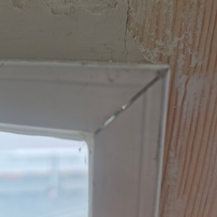 Närbild på hörnet av ett fönster med spricka och glipa mellan glas och karm, sliten vägg i bakgrunden.